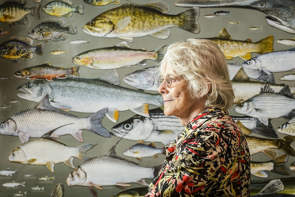 Kandis Elliot, emerita senior artist in the Department of Botany, is pictured on June 30, 2015, with a poster she created that features life-size illustrations of every fish species in the state of Wisconsin. The poster hangs outside her office in Nolan Hall at the University of Wisconsin-Madison. (Photo by Bryce Richter / UW-Madison)