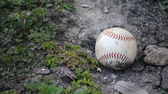 A well worn baseball sits in the dirt