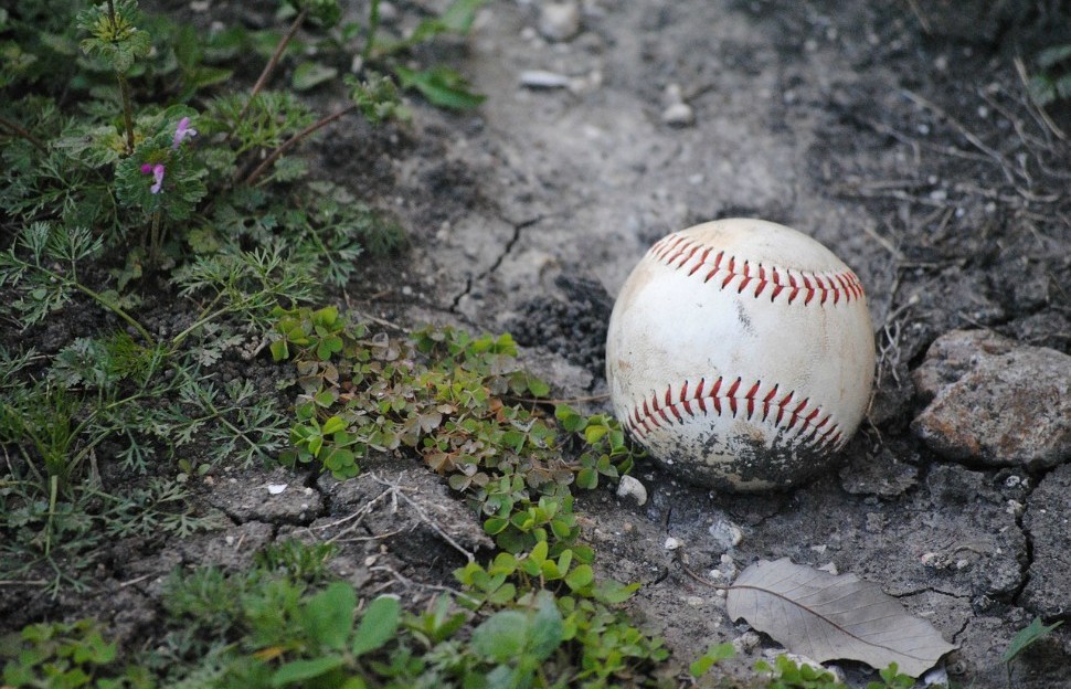 A well worn baseball sits in the dirt