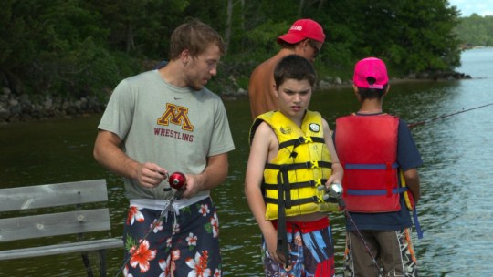 A University of Minnesoat student-athlete fishes with a camper at Camp Odayin