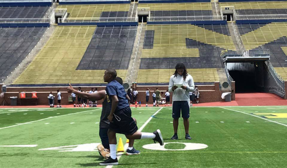 Students from the Youth Impact Program join University of Michigan football players on the field of the Big House stadium.
