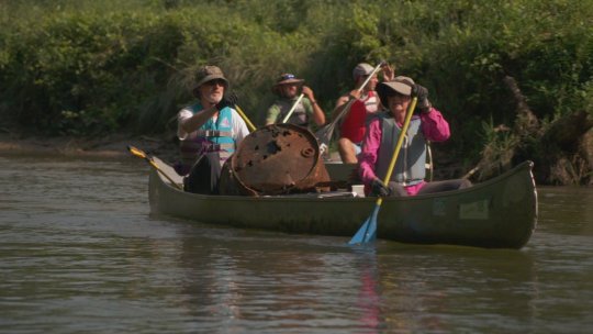 volunteers with Iowa project aware make their way down the a river with garbage collected in their canoe